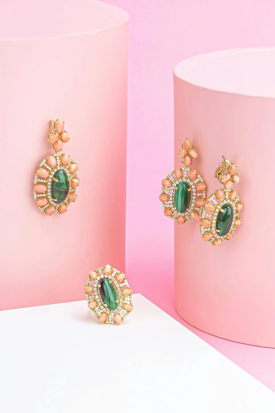 Gold earrings set with green stones, shown against a pink backdrop